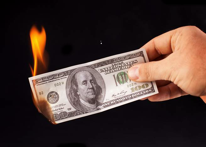 A hand holding a burning hundred-dollar bill